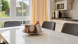 A dining table with a package on it, a window with curtains, and a kitchen area with appliances.