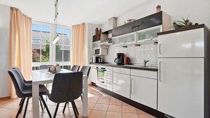 A modern kitchen with white cabinets, a dining table with chairs, a refrigerator, and a window with curtains.