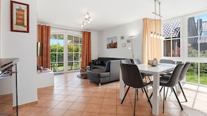 A modern living area with a sofa, dining table, chairs, and a large window offering a view of the outdoors.