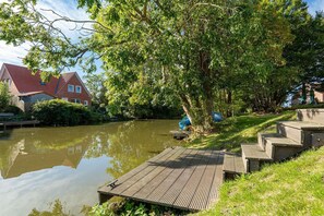 A riverside property with a wooden dock, a house with a red roof, and lush greenery.