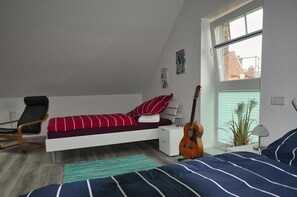 A bedroom with a bed, a chair, a guitar, and a window.