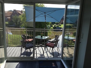 A glass-enclosed balcony with outdoor furniture, a view of a lake, and a clear sky.