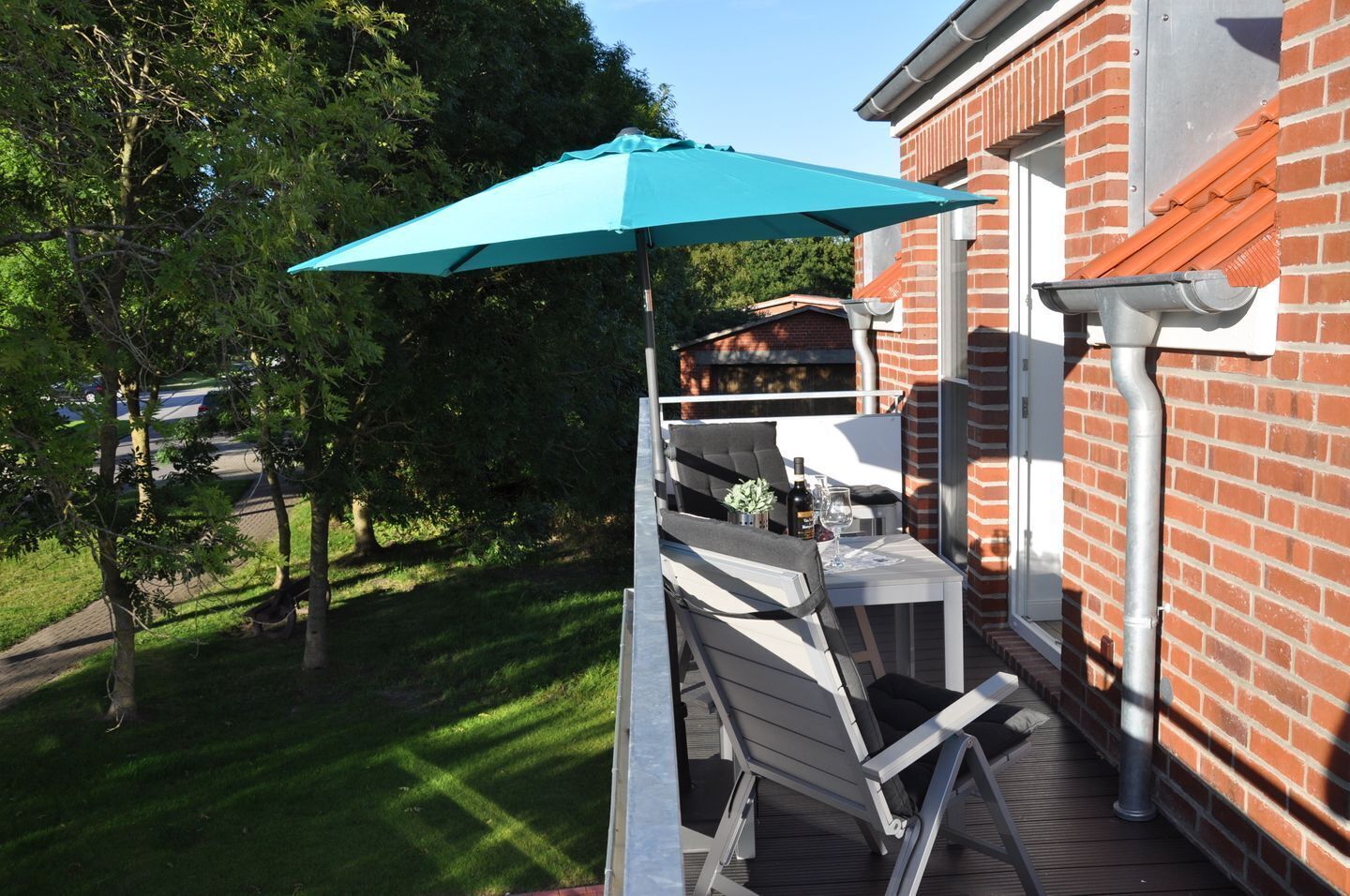 Eine Terrasse mit Tisch und Stühlen, einem blauen Sonnenschirm und einem Ziegelgebäude im Hintergrund.