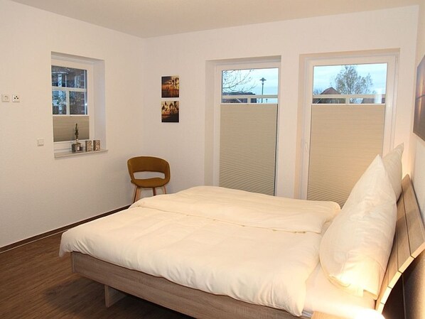 Une chambre à coucher avec un lit, une chaise et deux fenêtres.
