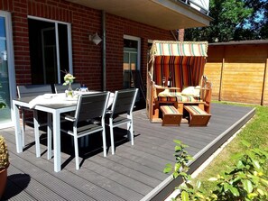 Une terrasse extérieure avec une table et des chaises, une plateforme en bois et un auvent à rayures.