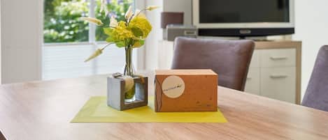 A wooden table with a vase of flowers and a cardboard box labeled 'Pro-Uraub' on a yellow placemat.