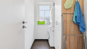 Une buanderie équipée d’un lave-linge, d’un étendoir et d’une fenêtre donnant sur des arbres.