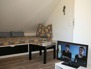 Et værelse med en seng, et lille bord og et fjernsyn, der viser et videoopkald.