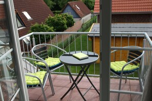 A balcony with two chairs and a small table, surrounded by a metal railing. - Kyana - Schöne Ferienwohnung in Ruhiger Lage von Norden (Norden)