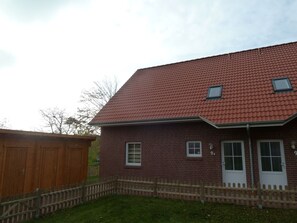 A two-story brick house with a red-tiled roof, a wooden fence, and a small shed in the background. - Kyana - Schöne Ferienwohnung in Ruhiger Lage von Norden (Norden)
