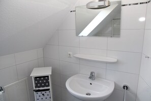 Een badkamer met een wit wastafelmeubel, een spiegel en een plank boven de wastafel.