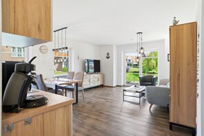 Ein modernes Wohnzimmer mit Holzboden, Essbereich, Fernseher und Blick ins Freie.