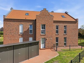 Un bâtiment de deux étages en briques, avec un toit recouvert de tuiles rouges, une entrée centrale et un espace extérieur clôturé.