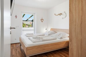 Une chambre moderne avec un lit en bois, du linge de lit blanc, une vue par la fenêtre et une porte avec une pancarte.