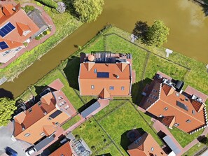 Vue aérienne d’un quartier résidentiel avec des maisons aux toits recouverts de tuiles rouges, un espace vert central et une rivière.