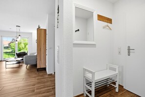 Une pièce moderne avec un plancher en bois, un banc blanc, une porte avec un miroir et une vue sur un jardin.