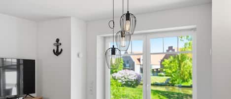 Uma sala de estar moderna com televisão, armário de madeira e vista para um jardim através de grandes janelas.