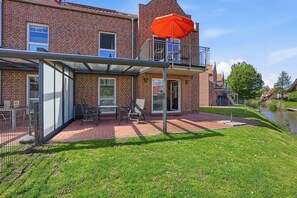 Une maison en briques avec un patio, des sièges d’extérieur et un parasol rouge.
