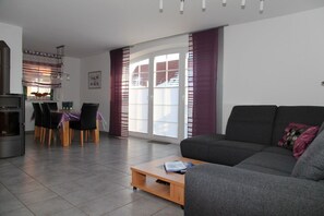 A modern living room with a grey sofa, a wooden coffee table, and a dining area with a table and chairs. - Achtern Diek - Holiday home with 100sqm for up to 6 persons with 2 bathrooms and (Norden)