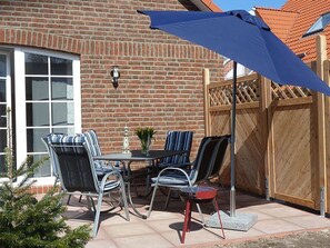 Une terrasse extérieure avec un mur en briques, une clôture en bois et une table avec des chaises.