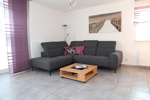 A modern living room with a grey sectional sofa, a wooden coffee table, and a painting of a bridge. - Achtern Diek - Holiday home with 100sqm for up to 6 persons with 2 bathrooms and (Norden)
