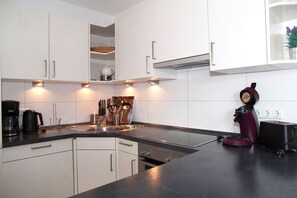 A modern kitchen with white cabinets, a black countertop, and a built-in oven. There is a coffee maker, a toaster, and a kettle on the counter.
