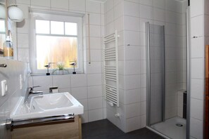A modern bathroom with a white sink, a window with a view, a shower, and a towel rack.