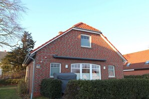 A two-story brick house with a sloped roof, a small window, and a covered outdoor seating area.