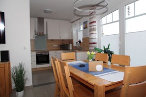 A modern kitchen with white cabinets, a microwave, and a sink. There is a dining table with chairs and a plant on the table.