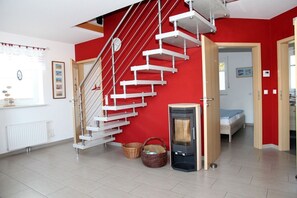 A modern interior with a red accent wall, a white staircase, a compact heater, and a bed in the adjacent room. - Achterhook - Allergikerfreundliches Ferienhaus in Norden (Norden)