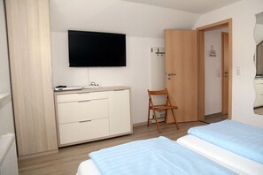 A bedroom with a bed, a TV mounted on the wall, a wooden chair, and a wardrobe. - Achterhook - Allergikerfreundliches Ferienhaus in Norden (Norden)
