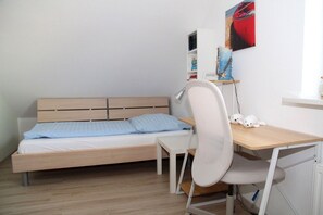 A small, neatly arranged bedroom with a single bed, a desk, and a chair.