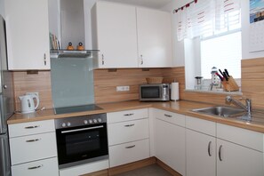A modern kitchen with white cabinets, a built-in oven, a microwave, and a sink.