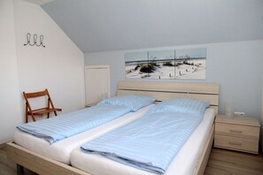 A bedroom with a double bed, a wooden nightstand, a chair, and a painting of a beach scene.