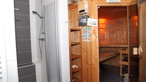 En bastu med en träpanel på utsidan, ett duschutrymme med grå kakelplattor och en kontrollpanel med olika knappar och en affisch.
