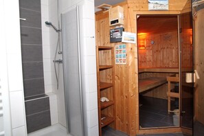 A sauna with a wooden exterior, a shower area with grey tiles, and a control panel with various buttons and a poster. - Achterhook - Allergikerfreundliches Ferienhaus in Norden (Norden)