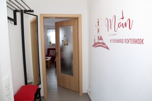 A hallway with a door leading to a dining area, a wall with a welcome sign, and a red bench.