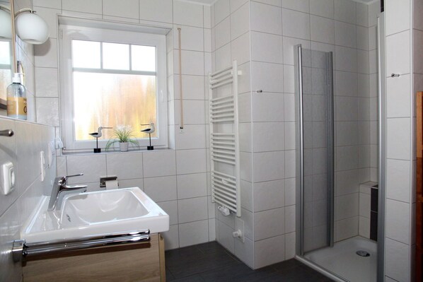 Une salle de bain moderne avec un lavabo blanc, une fenêtre donnant sur un beau paysage, une douche et un porte-serviettes.