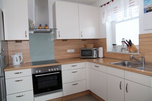 Una cocina moderna con gabinetes blancos, horno empotrado, microondas y fregadero.