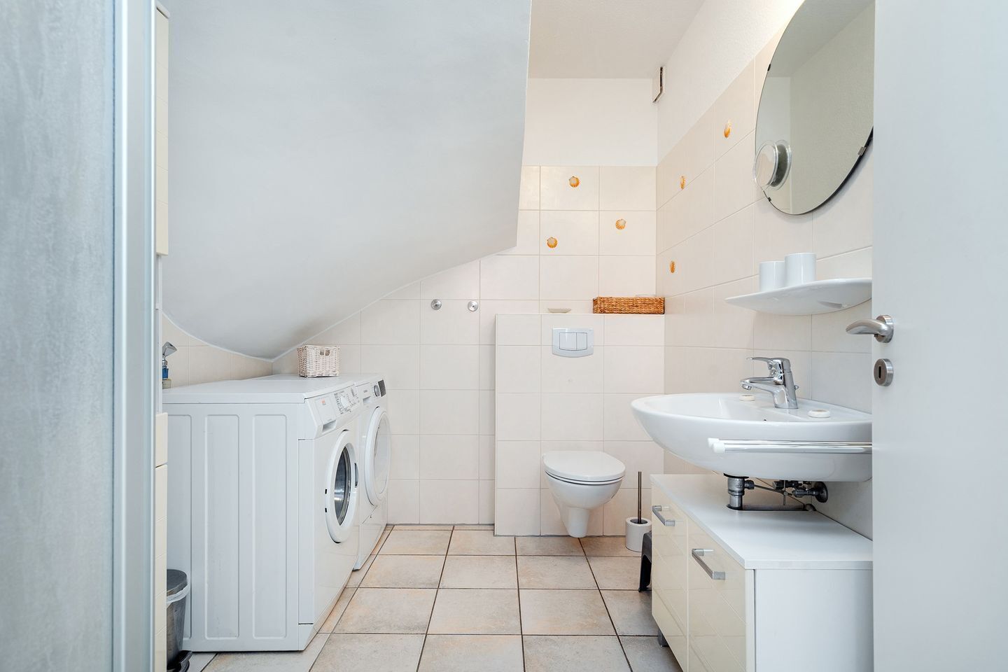 A compact, modern bathroom with a built-in washing machine, a toilet, and a sink with a mirror.
