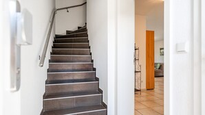 Una escalera con barandilla metálica que lleva a un cuarto con puerta de madera y suelo de baldosas.