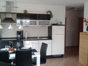 A modern kitchen with white cabinets, a black countertop, and a dining area with a table set for two. - Gesa - Komfortable Ferienwohnung im Grachtenviertel (Krummhörn)