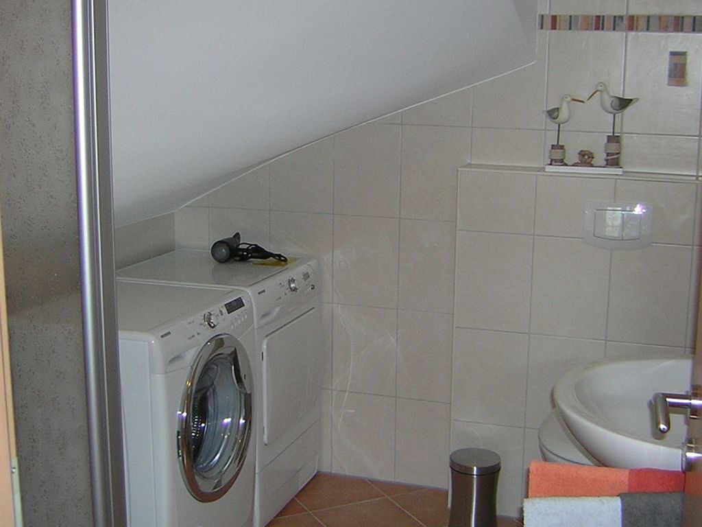 Ein kleiner Waschbereich mit Waschmaschine, Mülleimer und einem Badezimmer mit Waschbecken und Toilette.