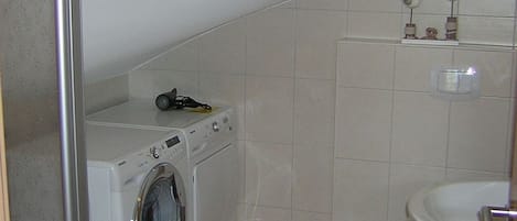 Ein kleiner Waschbereich mit Waschmaschine, Mülleimer und einem Badezimmer mit Waschbecken und Toilette.