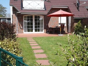 Una casa de ladrillo con un patio, un paraguas rojo y un jardín con piedras para pisar.