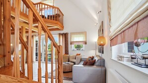 A modern interior with a wooden staircase, a grey sofa, and a dining area. - Friesenperle - Great vacation home (85sqm) for 4 people with fireplace directly on the (Krummhörn)