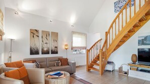 A modern living room with a sofa, coffee table, and a staircase. - Friesenperle - Great vacation home (85sqm) for 4 people with fireplace directly on the (Krummhörn)