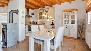 A modern kitchen with a central island, wooden ceiling beams, and white cabinetry. - Friesenperle - Great vacation home (85sqm) for 4 people with fireplace directly on the (Krummhörn)