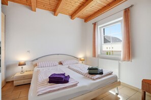 A bedroom with a bed, two bedside tables, a window with curtains, and a radiator.