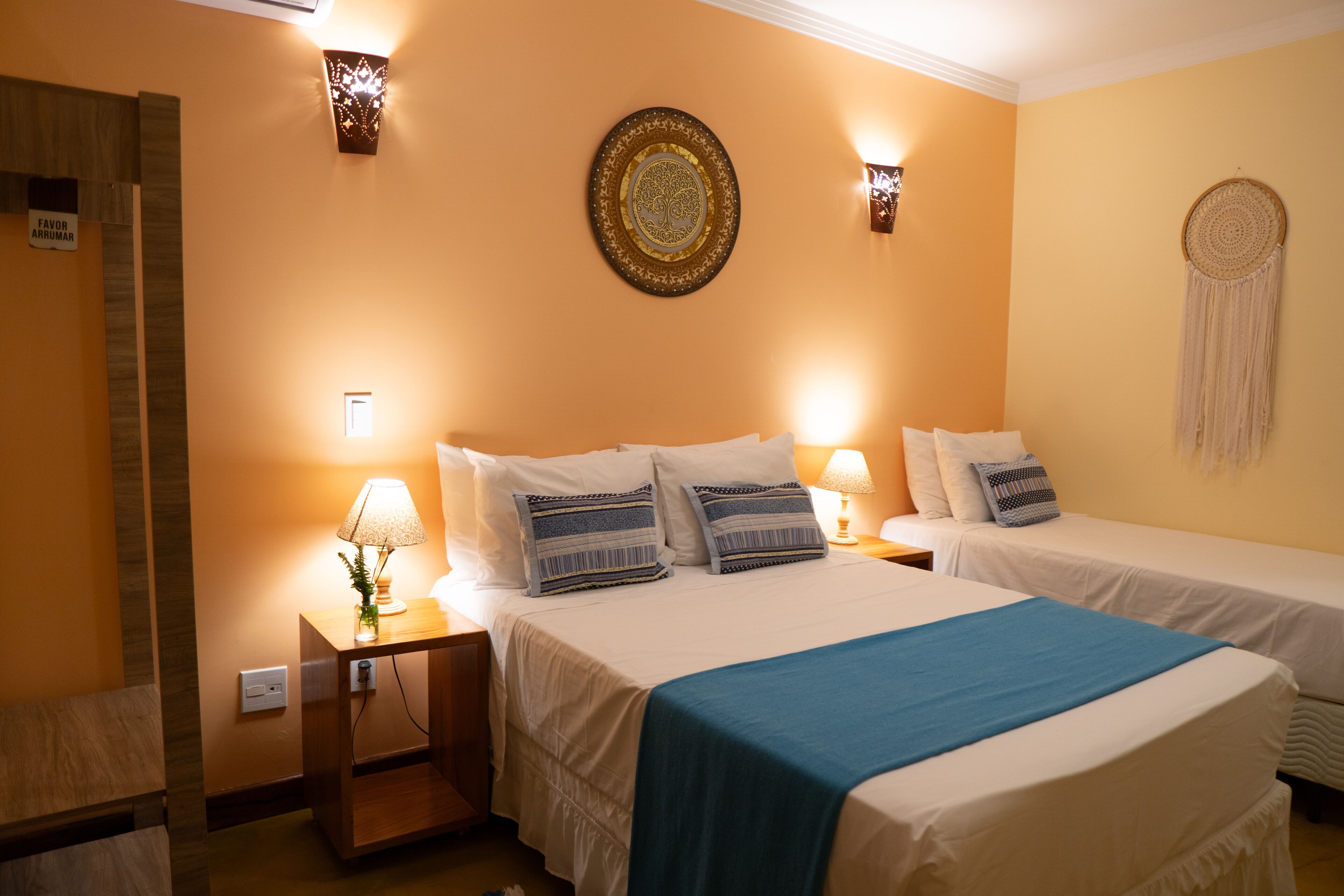 Une chambre d’hôtel avec deux lits, une table de chevet avec une lampe, une assiette décorative accrochée au mur et un attrape-rêves.